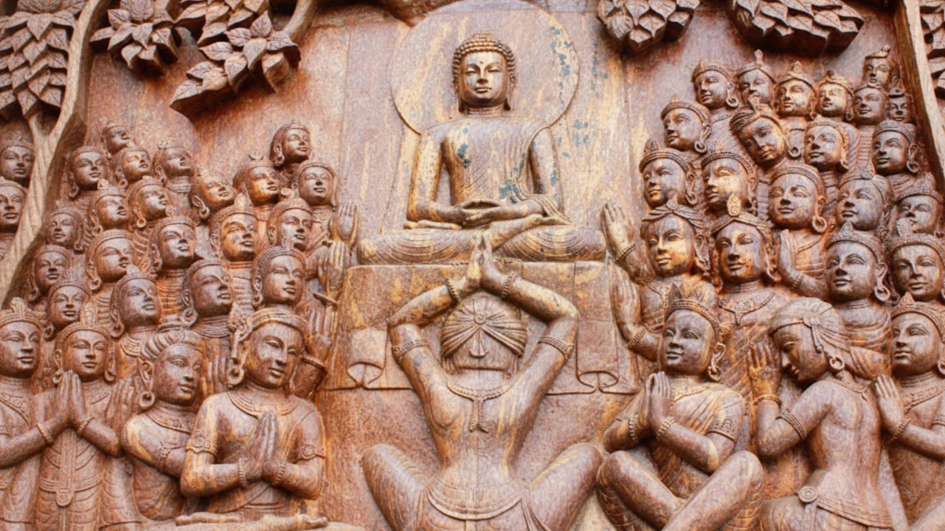 stone-carving-of-buddha-meditating-surrounded-by-devotees-in-prayer